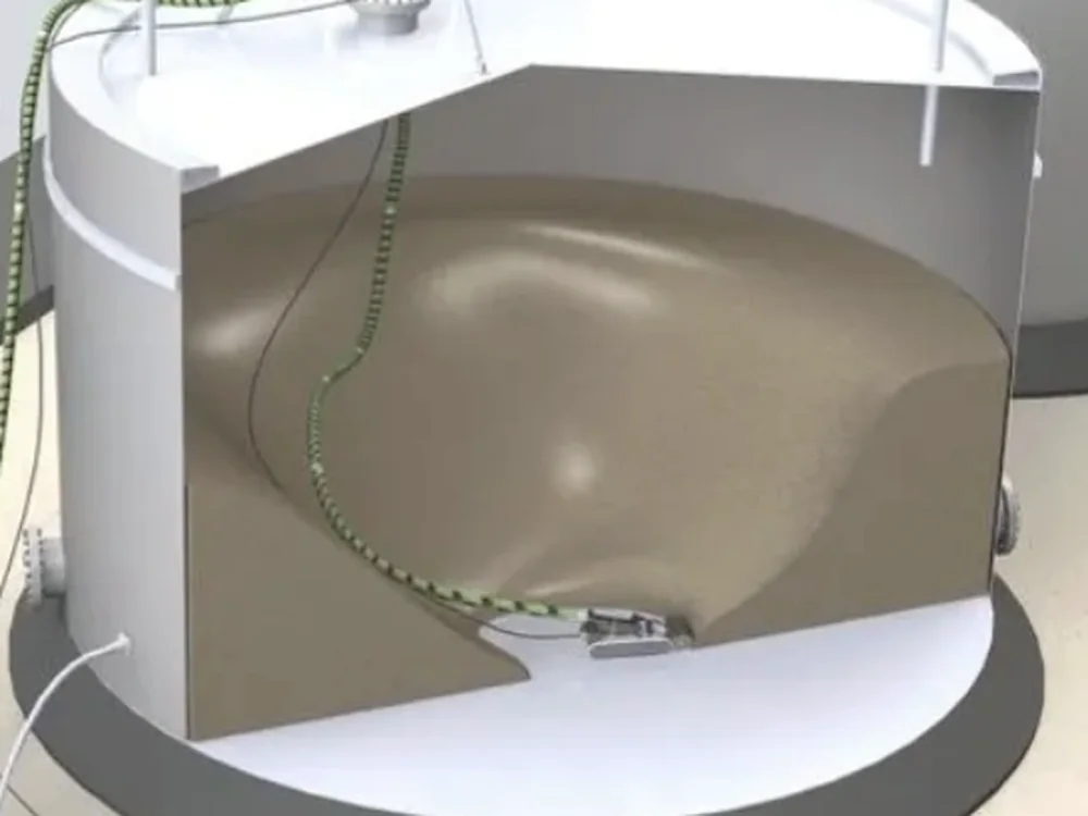 Cutaway visualisation of a storage tank, showing the crawler working on the floor beneath accumulated sediment with its umbilical run through the roof manway.